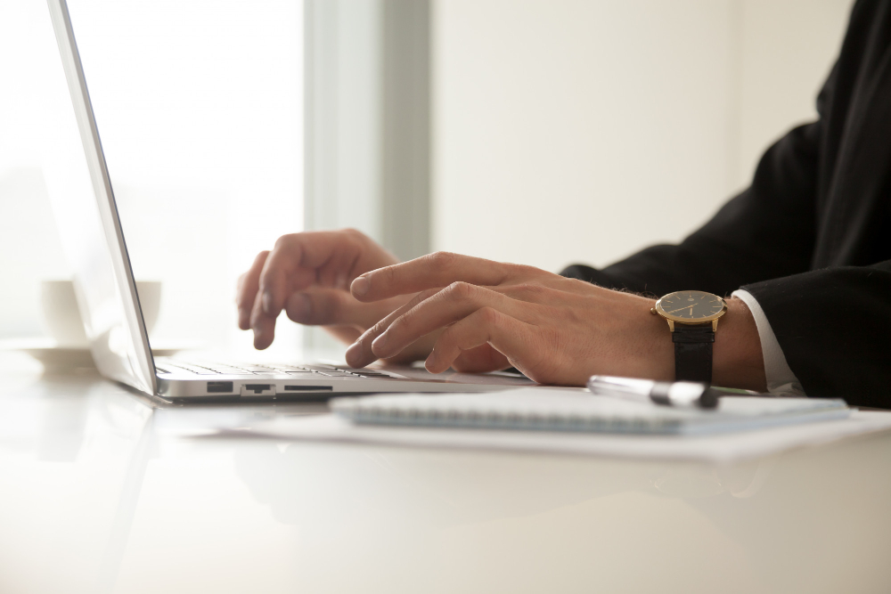 Close Up Image of Mans Hands in Wristwatch Typing on Laptop